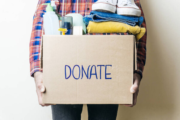CLOTHES DONATION AND FOOD DONATION CONCEPT. A man holding a donation box with clothes, shoes and hygiene products.