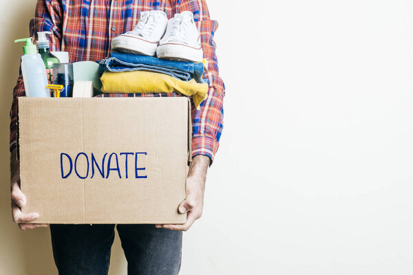 CLOTHES DONATION AND FOOD DONATION CONCEPT. A man holding a donation box with clothes, shoes and hygiene products. Copy space