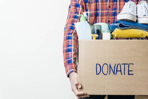 CLOTHES DONATION AND FOOD DONATION CONCEPT. A man holding a donation box with clothes, shoes and hygiene products. Copy space