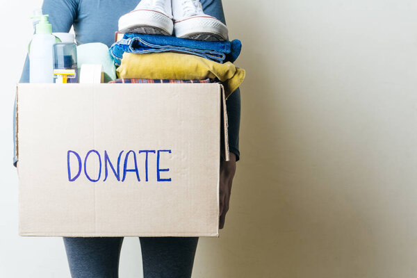 CLOTHES DONATION AND FOOD DONATION CONCEPT. A woman holding a donation box with clothes, shoes and hygiene products. Copy space