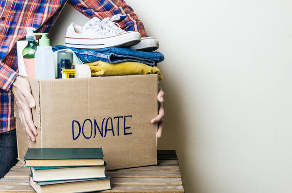 CLOTHES DONATION AND FOOD DONATION CONCEPT. A man holding a donation box with clothes, shoes and hygiene products. Copy space