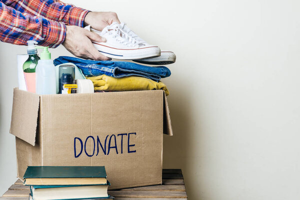 CLOTHES DONATION AND FOOD DONATION CONCEPT. A man holding a donation box with clothes, shoes and hygiene products. Copy space