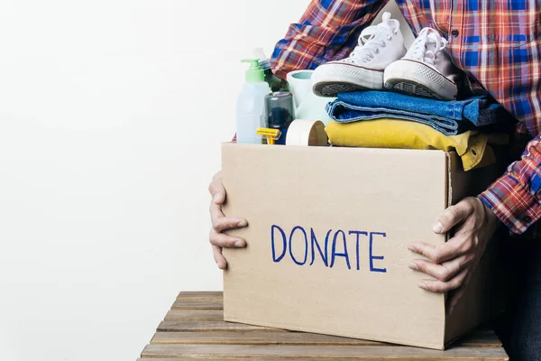 CLOTHES DONATION AND FOOD DONATION CONCEPT. A man holding a donation box with clothes, shoes and hygiene products. Copy space