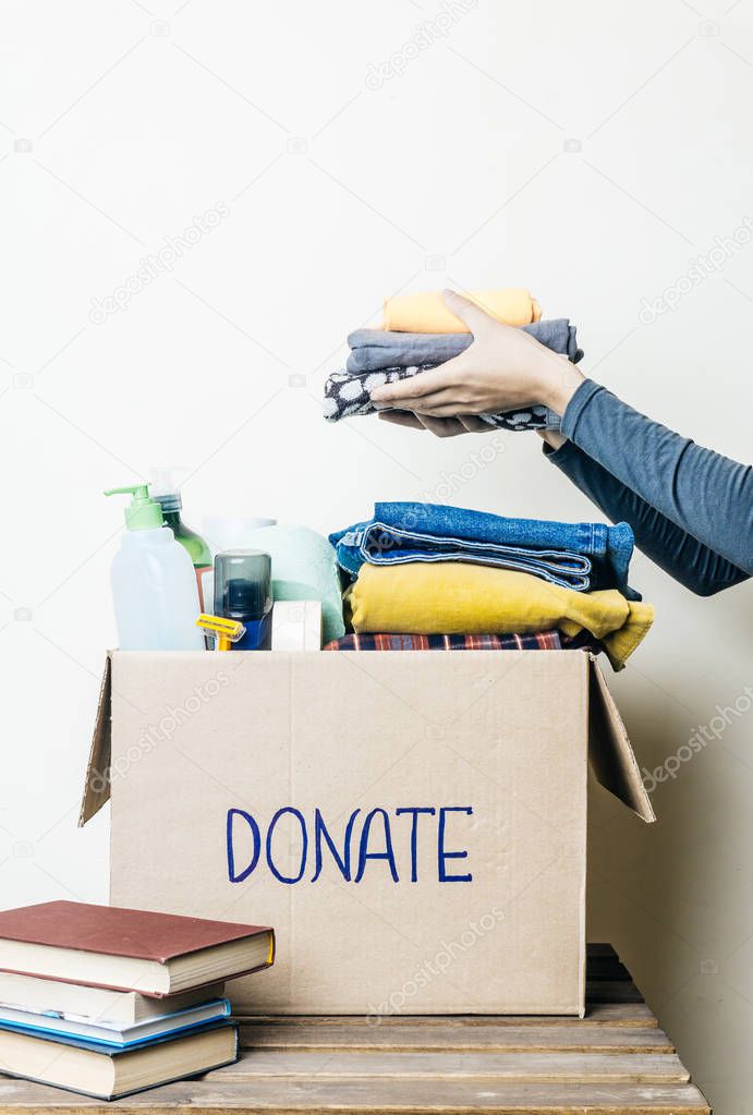 CLOTHES DONATION AND FOOD DONATION CONCEPT. A woman holding a donation box with clothes, shoes and hygiene products.