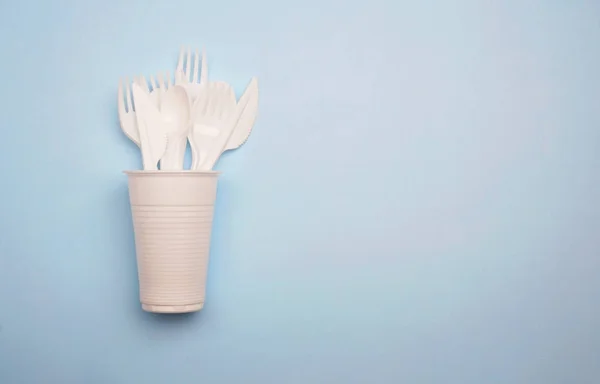 Single-use plastic products: plastic cutlery, cups on bright blu