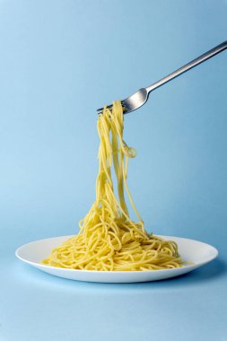 Beyaz tabakta çatallı spagetti makarna, mavi bir sırtüstü.