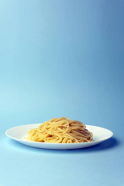 Spaghetti pasta på en hvid plade på en blå baggrund. Kreativ , - Stock-foto