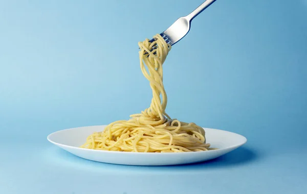 Spaghetti pasta with a fork on a white plate on a blue backgroun — Stock Photo, Image