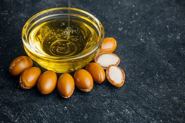 Koyu bir ahşap zeminde Argan tohumları ve yağı. Argan yağı bazlı kozmetik konsepti.