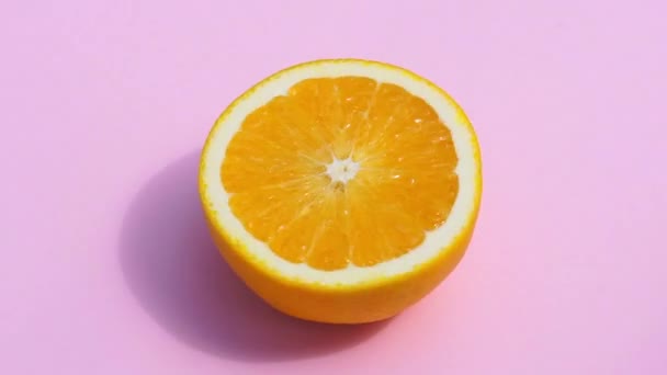 ピンクの背景にオレンジを回転させると隔離されます 夏の日差しの中で新鮮な黄色のオレンジを色のパステルカラーの背景でジューシーに フレッシュジュース フルーツ ビタミン 夏のコンセプト — ストック動画
