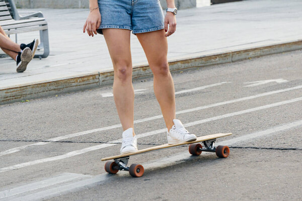 Young girl in shorts on a skateboard in the city. Rest and relaxation in the city in the summer. Lifestyle concept