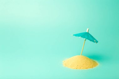 Tatil, yaz, rahatlama ve deniz konsepti. Renkli temiz bir arka planda kum ve şemsiyeli en az yaratıcı kompozisyon.