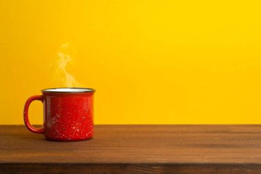 Sarı arka planda kırmızı bardak. Çay ya da ahşap bir masada kahve içmek için klasik bir bardak. Günaydın, yemek ve içki konsepti..