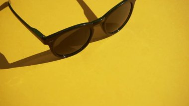 Güneş ışığında sarı bir arka planda güneş gözlüğü. Yaz, dinlenme ve rahatlama konsepti. En düşük düzlemli video