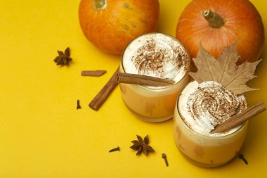 Balkabaklı latte içeceği. Baharatlı balkabağı aromalı sonbahar kahvesi ve sarı arka planda krema. Cadılar Bayramı ve Şükran Günü için Mevsimlik Sonbahar İçkileri