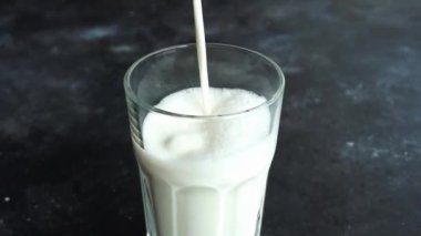 Süt koyu bir arka planda bir bardağa dökülüyor. Süt ve süt ürünleri.