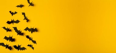 Cadılar Bayramı afişi. Sarı arka planda kağıttan kesilmiş siyah yarasalar. Bayram için Cadılar Bayramı dekorasyonu ve süslemeleri, kopya alanı.