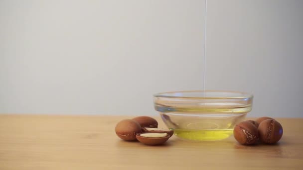 Argan olja häller i en glasskål med arganfrön på en vit bakgrund. Arganolja baserad kosmetika koncept. — Stockvideo