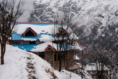 Kış manzarası. Karda ahşap ev. Bulanık arka planda kar kaplanmış dağ sırası.