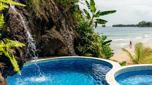 Голубой бассейн с видом на песчаный пляж с пышной растительностью на Боркас-дель-Торо, Панама, с одиноким человеком, идущим по шорлайну на краю океана — стоковое фото
