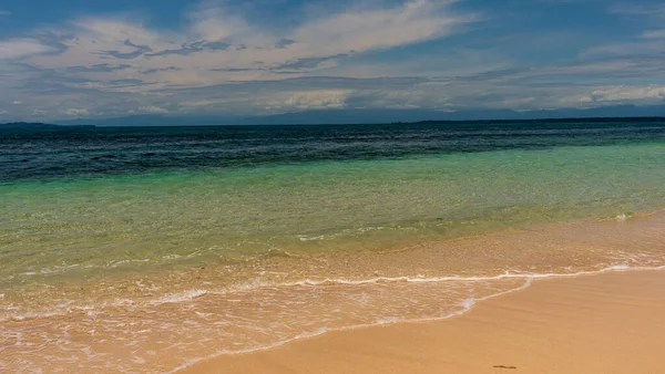 Panama, Bocas Del Toro 'daki Idyllic kumlu tropikal plajı sakin mavi okyanusuyla bulutlu mavi gökyüzünün altında, popüler bir turizm beldesi olan