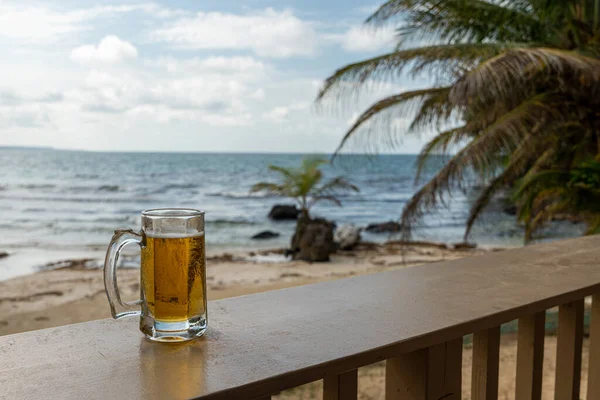 Холодная бутылка пива в стеклянной кружке с видом на море и пляж в Бокас-дель-Торо, Панама, в концепции летнего отдыха и путешествий — стоковое фото