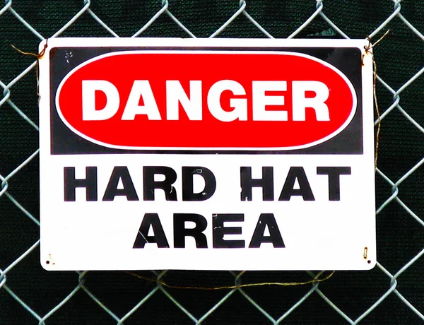 Danger hard hat area sign on a fence rend, white and black