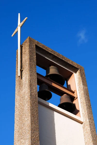 Community Episcopal Church Steeple made of brown and tan peables with a Gold Cross at the top and a blue sky and white clouds background.