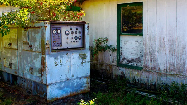 Abandonded old wood house on the side of the road with a propane control center attached to the back.