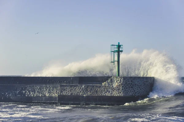 Huge wave and jetty pier with metal beacon. Water splashing during stromy weather.