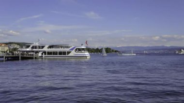 Zürih, İsviçre - 31 Mayıs 2019: Zürih Gölü 'ndeki tekneler, bir rıhtımdaki Zürih Gölü Navigasyon Şirketi gemisi, rıhtımdaki insanlar, arka plandaki Alpler' in zirveleri - Zürih şehrinin manzarası.