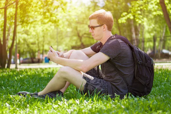 a man sits on the grass and looks at the phone