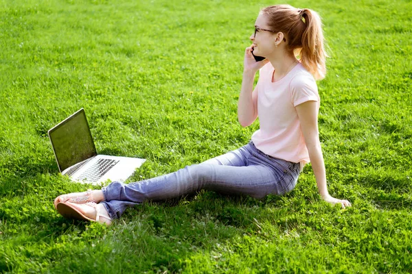 girl on the lawn with a laptop and talking on the phone