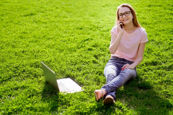 girl on the lawn with a laptop and talking on the phone