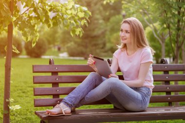 Kız parkta bir bankta oturmuş bir tablet ile