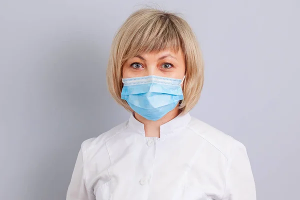 woman doctor in mask on grey background. copy space.