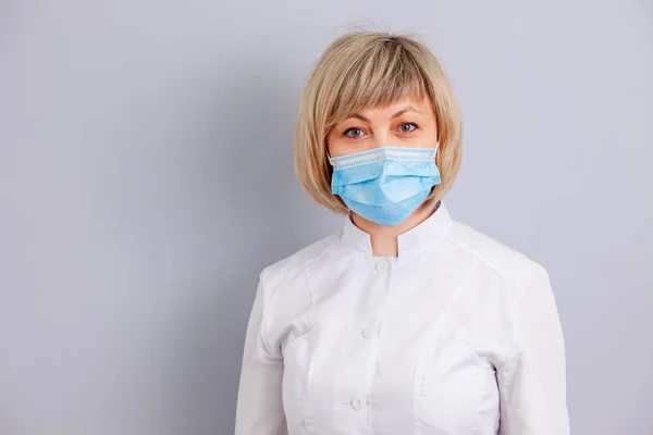woman doctor in mask on grey background. copy space.