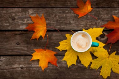 Arka plan eski koyu ahşap plakalar üzerinde kahve fincan kapuçino ve sonbahar yaprakları.