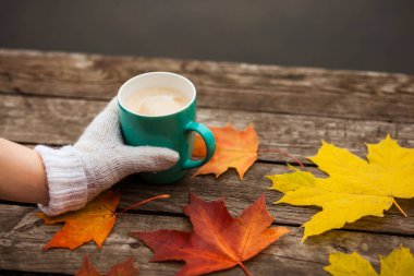 donmuş elinde kahve fincanı. arka planda sarı sonbahar yaprakları. Ahşap koyu arka plan üzerinde.