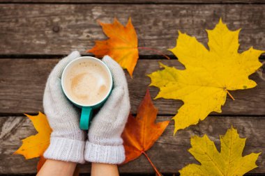 donmuş elinde kahve fincanı. arka planda sarı sonbahar yaprakları. Ahşap koyu arka plan üzerinde.