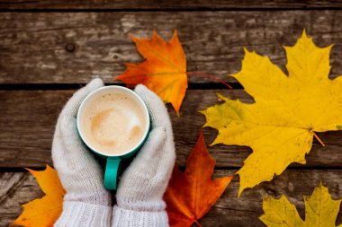 donmuş elinde kahve fincanı. arka planda sarı sonbahar yaprakları. Ahşap koyu arka plan üzerinde.