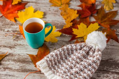 Bir fincan çay, sonbahar şapka, sarı ve kırmızı yaprakları. Ahşap arka plan üzerinde