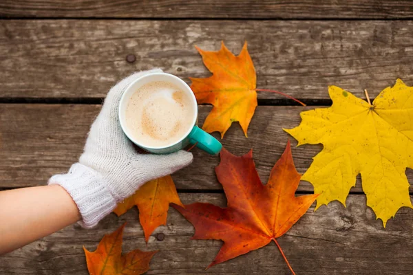 donmuş elinde kahve fincanı. arka planda sarı sonbahar yaprakları. Ahşap koyu arka plan üzerinde.
