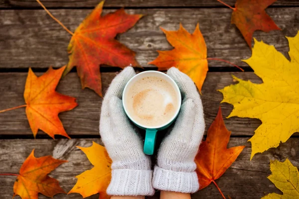 donmuş elinde kahve fincanı. arka planda sarı sonbahar yaprakları. Ahşap koyu arka plan üzerinde.