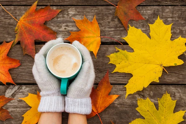 donmuş elinde kahve fincanı. arka planda sarı sonbahar yaprakları. Ahşap koyu arka plan üzerinde.