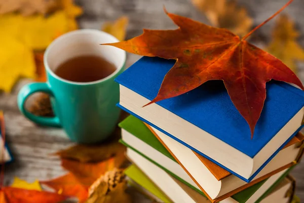 Sonbahar. Kitap. Bir fincan çay. Sarı kırmızı yapraklar. Ahşap arka plan