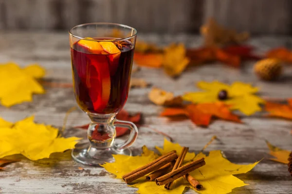 Sıcak Mulled şarap. Sonbahar arka plan üzerinde. Turuncu tarçın kırmızı şarap cam. Alkol. Sarı kırmızı yaprak. Ahşap koyu arka plan üzerinde.