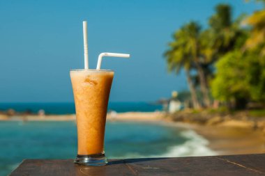 Deniz ve palmiye ağaçlarının arka plan üzerine taze meyve suyu ile cam