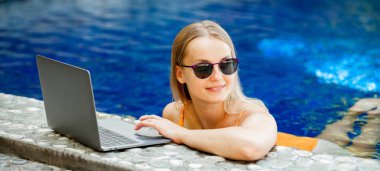 bir dizüstü bilgisayar ile çalışma havuzunda güneş gözlüklü kız