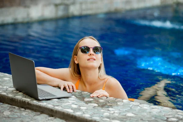 bir dizüstü bilgisayar ile çalışma havuzunda güneş gözlüklü kız